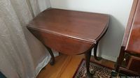 Wooden drop leaf table with one leaf folded down showing curved leg design.