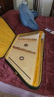 Open hard case with plush lining showing trapezoidal wooden dulcimer with dual bridges and metal strings.