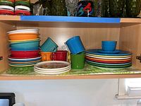 Wide shelf view showing stacks of Fiesta Ware colorful plates and bowls, with matching mugs in front.