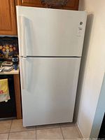 Front view of white GE top freezer refrigerator with handles and closed doors.