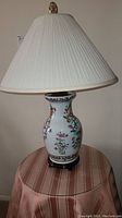 Close-up of one ceramic table lamp showing the floral design on the base, pleated cream shade, and wooden stand.