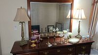 Two matching table lamps on a wooden dresser topped with other decorative items and a large mirror on the wall.