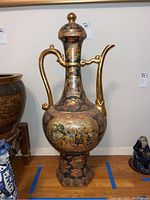 Full view of large Asian ceramic teapot with gold handle and spout, detailed painted scenes on body and base