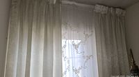 Full view of solid cream curtain panels hung over window with layered sheer embroidered curtains visible behind them.