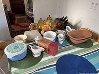 Overview of various vintage kitchen and serving items on table including Pyrex dish, bowls, canisters, gravy boat, cookie jar, cutlery and utensils.