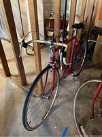 Front three‐quarter view showing red frame, drop handlebars with white tape, front caliper brake and wheel