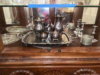 Wide view showing entire set on wooden sideboard with mirror background, including silver plate pots, creamer, sugar bowl, large tray, coasters, candlestick holders, and glass trays.