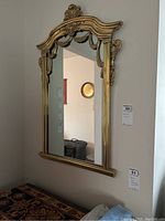 Full front view of the gilded framed wall mirror hanging on the wall with visible decorative elements and size tags.