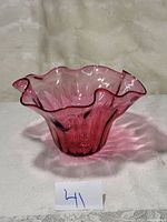 Front-left angle showing the ruffled pink glass bowl on a fabric surface.