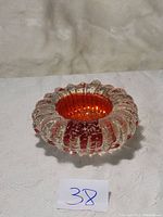 Photo of a decorative glass bowl with clear glass exterior and red glass interior, featuring wavy rounded shape and vertical ridged texture