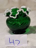 Photo of an emerald green Fenton glass rose bowl with snow crest white crimped rim on a beige surface, tagged with number 42.