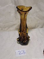 Amber glass vase with organic sculptural shape on white fabric background, labeled with number 23.