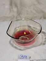 Clear glass bowl with red fade from center to edges, organic wavy square shape, photographed on neutral fabric background with inventory number sign.