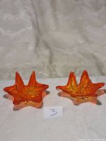Pair of bright orange star-shaped glass bowls on fabric surface with measuring note