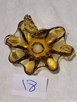 Top view of the amber seashell-shaped hand blown glass ashtray on a white lace background with a lot number card.
