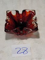 Front and above angle view of a red-amber Murano glass bowl with ruffled edges and flower-like form.