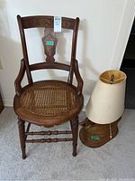 Front view of vintage wooden side chair with cane seat and carved back inlay, next to a wood base loon lamp with shade.