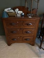 Front view of the wooden cabinet showing three drawers with carved wooden pulls and keyhole, worn top surface.