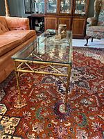 Side angled view showing bamboo-style metal frame and glass top on a Persian oriental rug indoors.