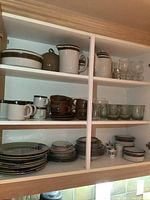 Shelf with mixed dishes including pottery mugs, plates, glassware, and small casserole dishes
