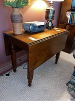 Full view of the wooden drop leaf table with one leaf folded down, showing the tabletop, legs, and some items placed on top.