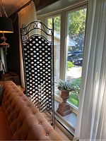 Full view of one panel of black metal lattice folding screen with decorative scrolling top edge.