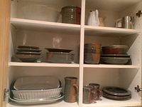 Overview of cabinet shelf with clear plastic bowl, brown/grey bowls and white pitchers