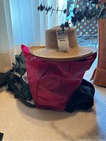 Photo showing magenta reusable shopping bag topped with small woven straw hat with lot tag