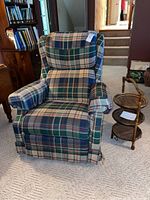 Plaid La-Z-Boy rocker recliner chair positioned beside the three-tiered woven wood tray table on a light carpet.