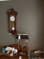 View of the Spirit wall clock mounted on the wall above the wooden table with the brass lamp in front and various decor items on the table.