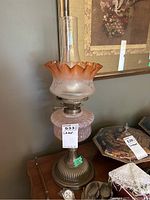 Full view of the oil lamp showing the tinted glass with orange fluted top, clear chimney, frosted glass base, and brass metal stand.