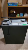 Front view of Staples paper shredder, rectangular black body with power cord wrapped around.