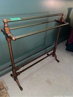 Full view of the quilt rack with brass rails and wooden frame against a green wall