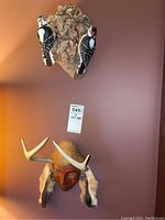 Two carved painted woodpeckers mounted on bark trunk and carved wood mask with antlers and fur hanging below
