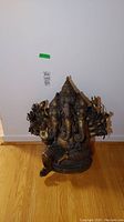 Full frontal view of brass Ganesha statue on hardwood floor against white wall