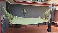 Green textile hammock hanging between two posts outdoors, showing full length and rope ends.