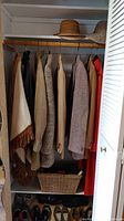 Closet shelf with woven sun hats and coats hanging on wooden hangers below, basket on bottom shelf, women's shoes on floor of closet.