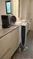 View of Bionaire tower fan with remote, black Honeywell heater and white surround heater on countertop