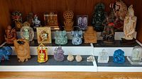 Group shot of all Indian stone, glass, and ceramic figurines arranged on stepped display trays, showing multiple small and medium sized figures including elephants, deities, and symbolic figures in various colors and materials.
