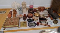 Full lot overview showing multiple Indian and brass figurines, trinket boxes, a candle hurricane lamp, decorative plate, and small game set arranged on floor.