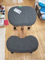 Top view of the chair with two gray fabric cushions: contoured backrest and rectangular seat, showing wood frame and caster wheels on hardwood floor.