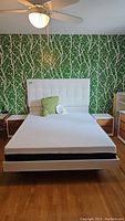 Front view of bed frame with mattress, headboard and side nightstands visible against patterned wallpaper