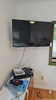Samsung 40 inch TV mounted on wall with cords hanging and electronic devices on a cabinet below.