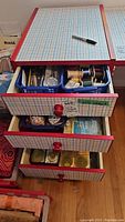 Full view of three drawers with sewing supplies inside, including scissors, threads, buttons, pins, lined with patterned paper.