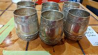 Group of six stamped silver cups on wood surface