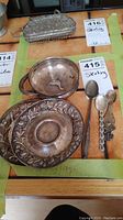 Poole sterling bowl with handle, two decorative saucers, and three sterling spoons with varying designs, displayed on a table