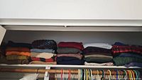 View of folded knit sweaters stacked on a top shelf of a closet, showing multiple colors and patterns.
