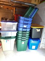 Stack of various plastic storage totes in green, blue, black, clear, beige, and white colors, most with lids