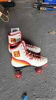 Full view of the pair of white leather Hang Ten roller skates with red, orange and yellow stripes and red wheels.