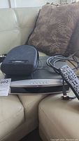 Bose Media Center unit with remote control and black carrying case for headphones on a couch.